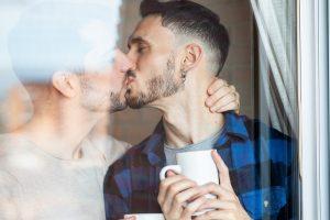 Dois homens se beijando segurando uma xícara de café